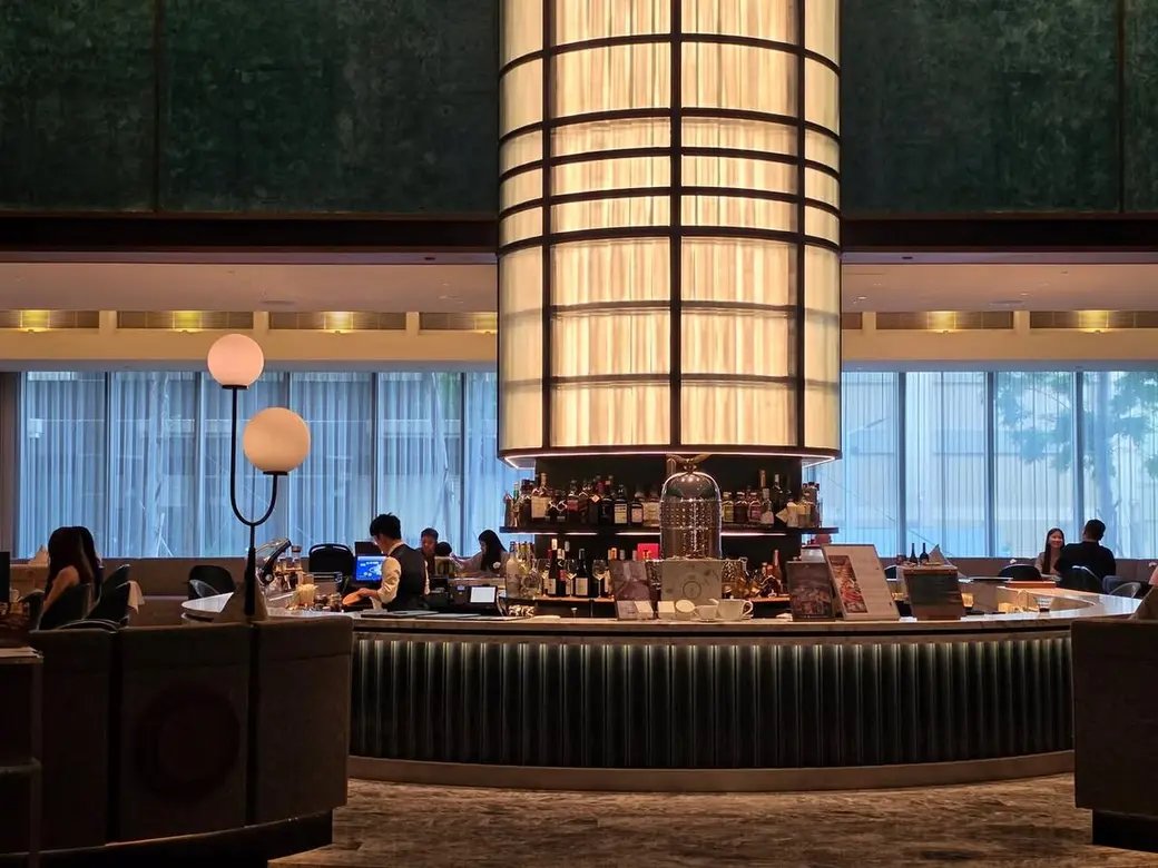 室內照片，飯店大廳酒吧中央是一根包著格柵燈罩的發光圓柱，四周是沙發座位與落地窗。